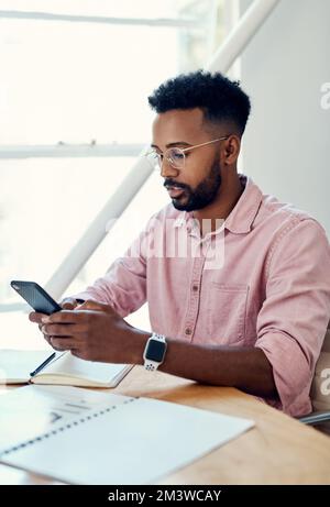 Updating my online calendar. a handsome young businessman sitting alone and using his cellphone in the office. Stock Photo