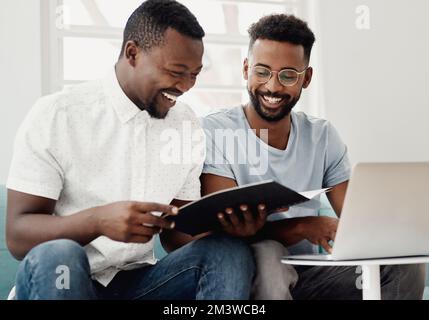 Bringing some positive energy to the workplace. two handsome businessmen sitting together and reading paperwork while using a laptop in the office. Stock Photo