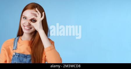 Girl search perfection. Charming pretty glad redhead female student assuring everything ok showing okay sign eye look through smiling delighted Stock Photo