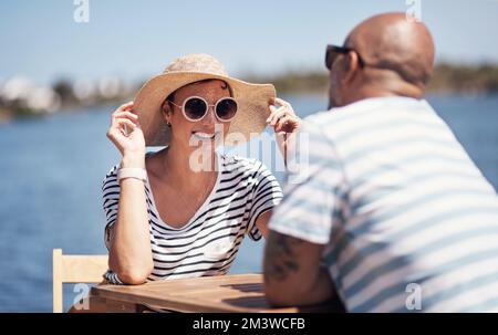 Do you like my hat. a cheerful young couple having a lunch date outside next to a beach promenade. Stock Photo