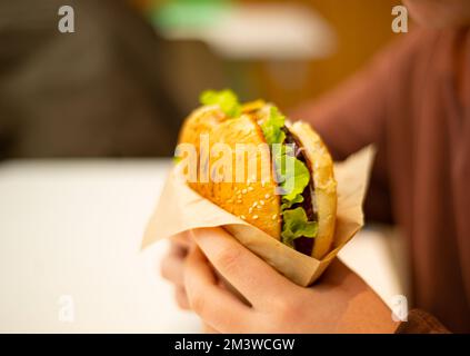 Burger in hand. Bun with sesame seeds. Green leaf lettuce. Vegetables and cheese. Stock Photo
