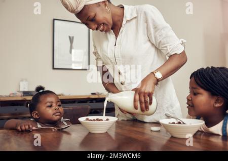 Start your mornings with a healthy and tasty meal. a young mother preparing cereal for her two adorable young daughters at home. Stock Photo