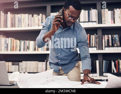 Are you sure those details are correct. a handsome young male architect taking a phonecall while working with blueprints in a modern office. Stock Photo