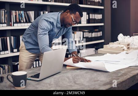 Paying attention to details. a handsome young male architect working with blueprints in a modern office. Stock Photo