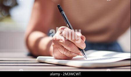 Retirement has given her the time to work on her book. an unrecognizable senior woman writing in her book outside on the balcony at home. Stock Photo