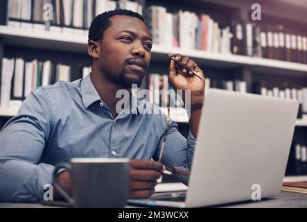 I gotta put some thought into this. a handsome young male architect looking thoughtful while working on a laptop in a modern office. Stock Photo