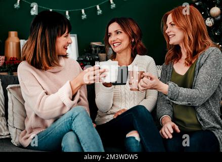 Heres to us ladies. three attractive middle aged women seated on a sofa together while drinking coffee at home during Christmas time. Stock Photo