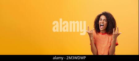 Waist-up shot of amazed happy stylish african american woman feeling awesome rocking on party yelling from joy and satisfaction showing rock n roll Stock Photo