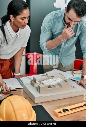 Getting their creative juices flowing. two architects working together on a scale model of a building in an office. Stock Photo