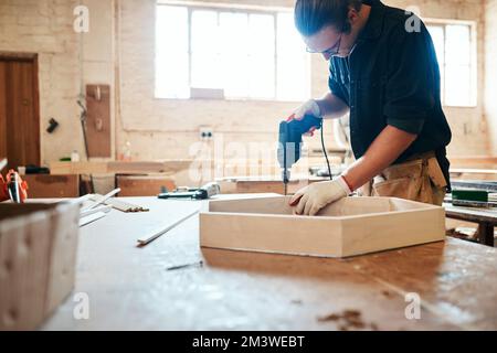 Just making some final adjustments to the masterpiece. a handsome young carpenter using an electric drill while working inside a workshop. Stock Photo