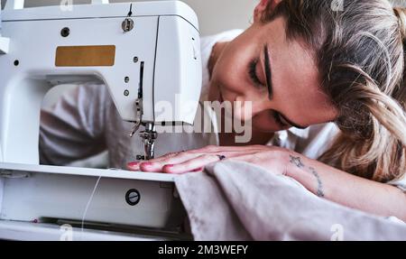 Adventure begins when you enter your sewing room. a young fashion designer using a sewing machine in her workshop. Stock Photo