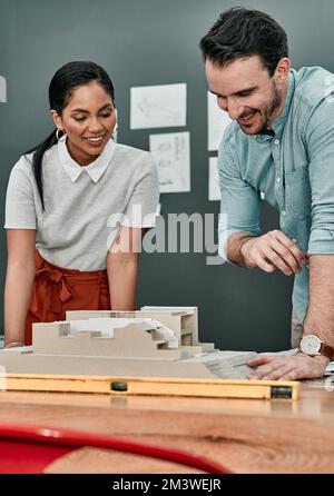 Every design needs dedication to grow into something bigger. two architects working together on a scale model of a building in an office. Stock Photo