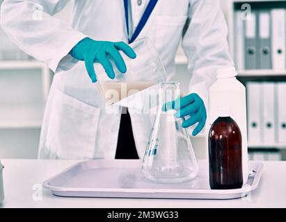 Setting up her experiment...an unrecognizable female scientist transferring a liquid from a beaker to a conical flask while working in a laboratory. Stock Photo