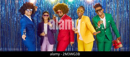 Happy friends or colleagues dancing with glasses of champagne at themed New Year's disco party. Stock Photo
