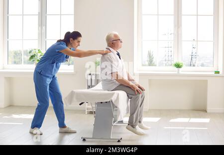 Senior man with back pain sitting on massage table while physiotherapist examines him Stock Photo