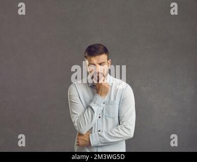 Serious puzzled sad man thinking looking down keeping fist at chin studio shot Stock Photo