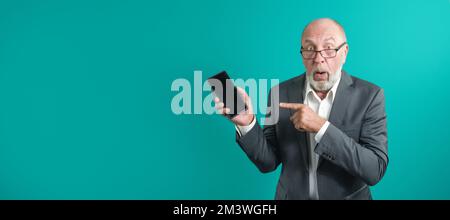 Application advertising. Adult man in glasses showing black blank smartphone screen recommending website posing in studio green background Stock Photo