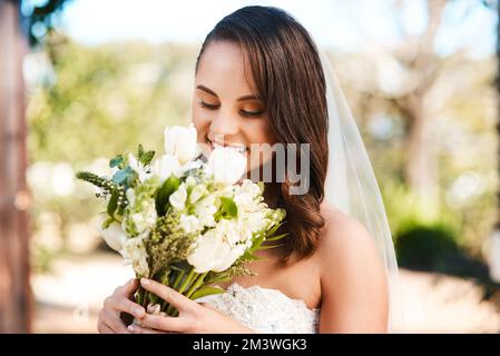 Such a beautiful scent. a beautiful young bride smiling while holding a bouquet of flowers on her wedding day. Stock Photo
