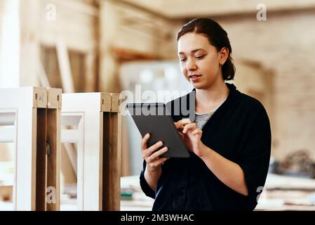 My tablet is my favorite tool in the workshop. a young female carpenter using a digital tablet while working inside her workshop. Stock Photo
