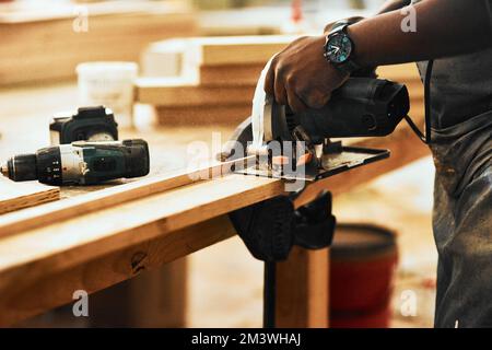 Power tools help increase productivity in your workshop. an unrecognizable carpenter using a circular saw to cut wood inside a workshop. Stock Photo