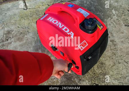 I start the gasoline inverter generator by hand, the red body has Honda written on it. Energy accident in Ukraine due to the war Stock Photo