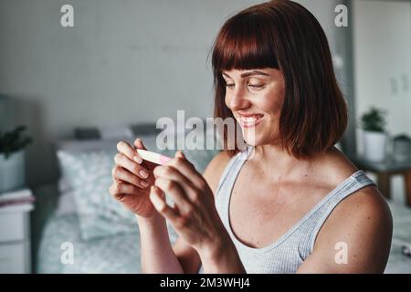 She cant wait to become a mom. an attractive young woman feeling happy while looking at her pregnancy test results at home. Stock Photo