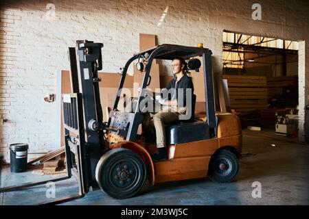 Every warehouse needs a forklift. a young male warehouse worker driving a forklift. Stock Photo
