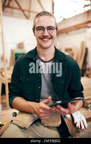 This device is my little assistant around here. Portrait of a handsome young carpenter using a digital tablet while working inside his workshop. Stock Photo