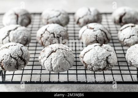 Chocolate chip cookies with cracks. Metallic rack with fresh baked chocolate crinkle cookies in icing sugar on white textured background. Vertical ori Stock Photo
