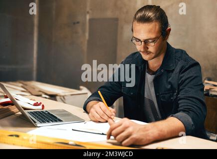 Time to draw everything out. a focused young male carpenter working on a project inside of a workshop at night. Stock Photo