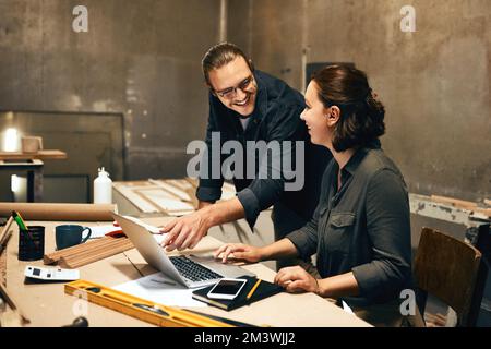 So you created this design. two cheerful young carpenters working on a project together while using a laptop inside of a workshop at night. Stock Photo