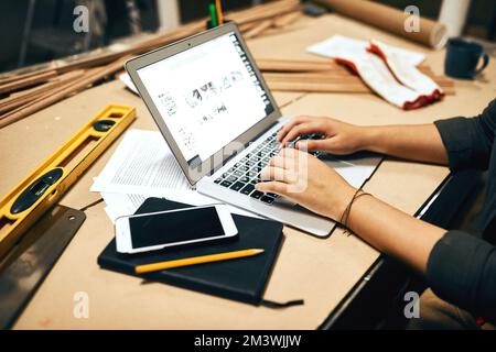 Working hard today. an unrecognizable female carpenter working on her laptop inside of a workshop at night. Stock Photo
