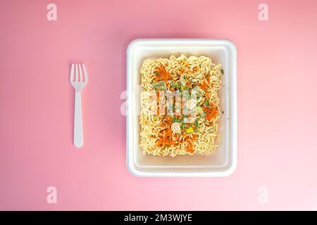 Dried Instant Noodles in Plastic Box on the pink table. top view Stock Photo