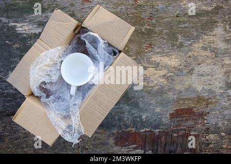 Packed cup in a plastic bubble wrap on an old wooden background. Fragile package. Stock Photo