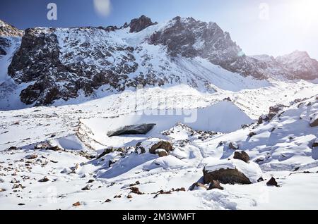 Man with backpack in at the snow frozen lake near big ice cave with beautiful mountains against blue sky in Almaty, Kazakhstan Stock Photo