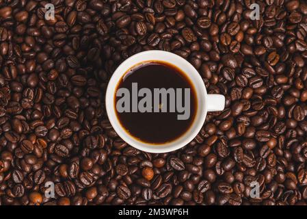 White cup of coffee surrounded by a background of roasted coffee beans. Stock Photo