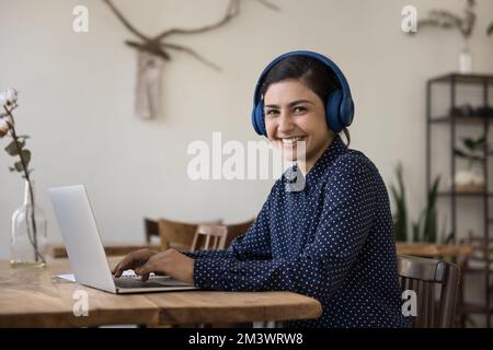 Cheerful beautiful Indian student woman wearing wireless headphones using laptop Stock Photo