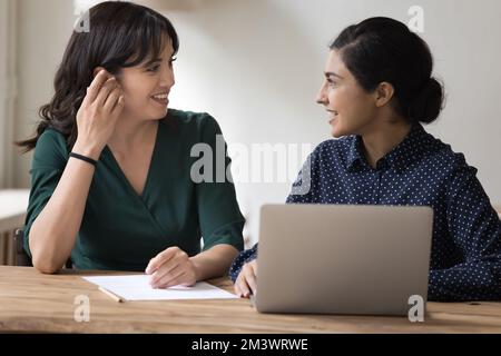 Happy multiethnic female office friends talking at workplace Stock Photo