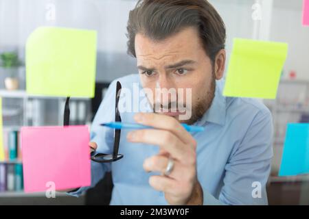 thoughtful man reading sticky notes in office Stock Photo