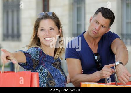 frustrated boyfriend pointing at his watch towards shopaholic girlfriend Stock Photo