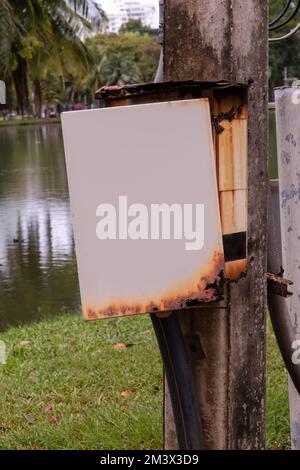 Rusty electric box with a blank  openeddoor next to a lake in a park Stock Photo