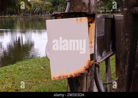 Rusty electric box with a blank  openeddoor next to a lake in a park Stock Photo