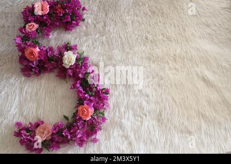 Number five, Shape of the number five with bougainvillea and rose flower on white fluffy blanket with empty area. Stock Photo
