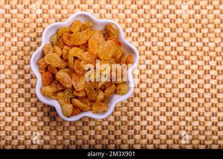Yellow golden raisins in white ceramic bowl on golden background. Stock Photo