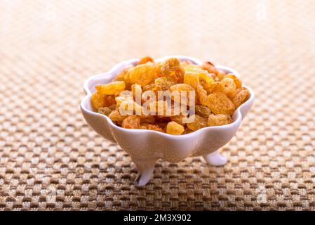 Yellow golden raisins in white ceramic bowl on golden background. Stock Photo