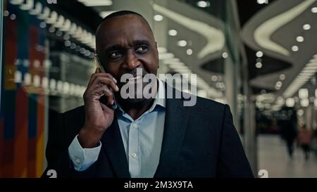 Smiling cheerful African middle-aged man entrepreneur businessman talk phone has work business friendly discussion negotiation networking with Stock Photo