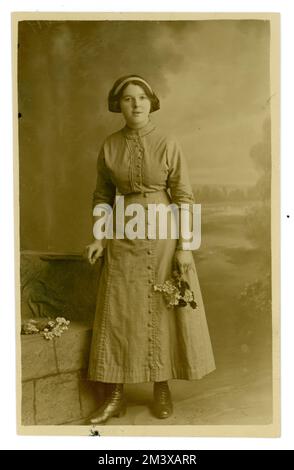 Original WW1 era portrait postcard of attractive late teens girl / young woman, wearing a blouse and long skirt, hemline just above her ankle, her hair seems to be tied up in a bow at the back, possibly her first grown up photograph. U.K, circa 1915. Stock Photo