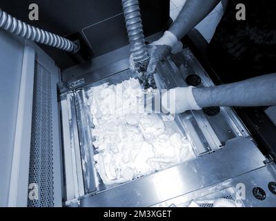 Mane taking out models from white polyamide powder in working chamber of 3D printer, cleaning and removes powder. Process of creating model on powder 3D printer. Multi Jet Fusion MJF. Worker hands Stock Photo