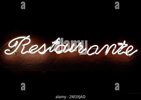 An orange neon sign saying 'Restaurants' in Madrid Spain isolated on an empty dark background Stock Photo