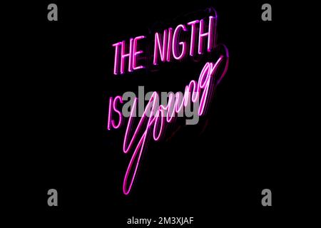 A pink neon sign saying 'The night is young' in Madrid Spain isolated on an empty dark background Stock Photo